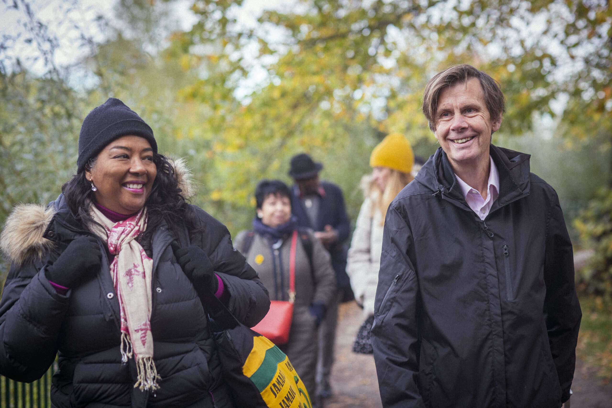 A man and a woman are walking in front of a small group of people in a park, they are laughing and smiling